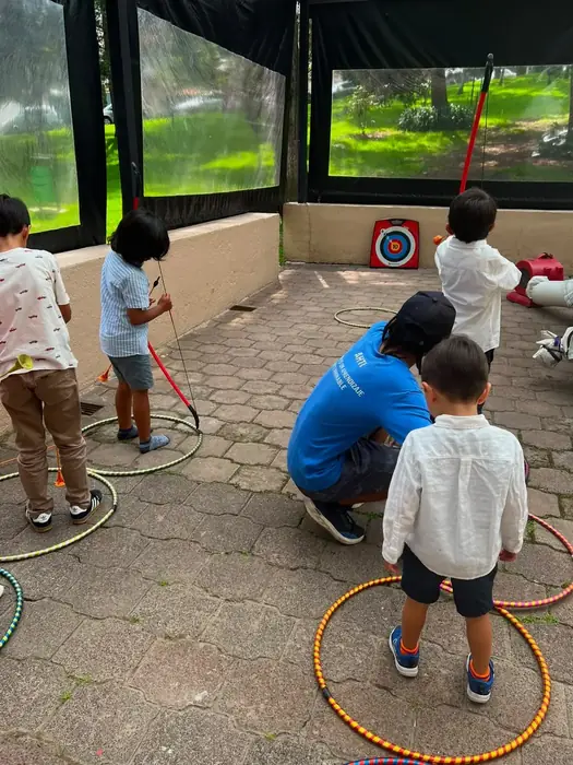 Niños practicando tiro con arco dentro de aros de colores, durante una fiesta con Tribu
