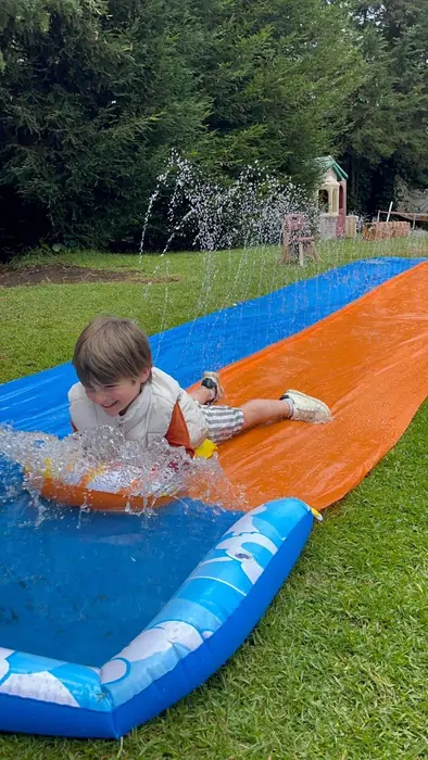 Niño de espaldas deslizándose por una resbaladilla de agua sobre el pasto, en un Fun Day de Tribu